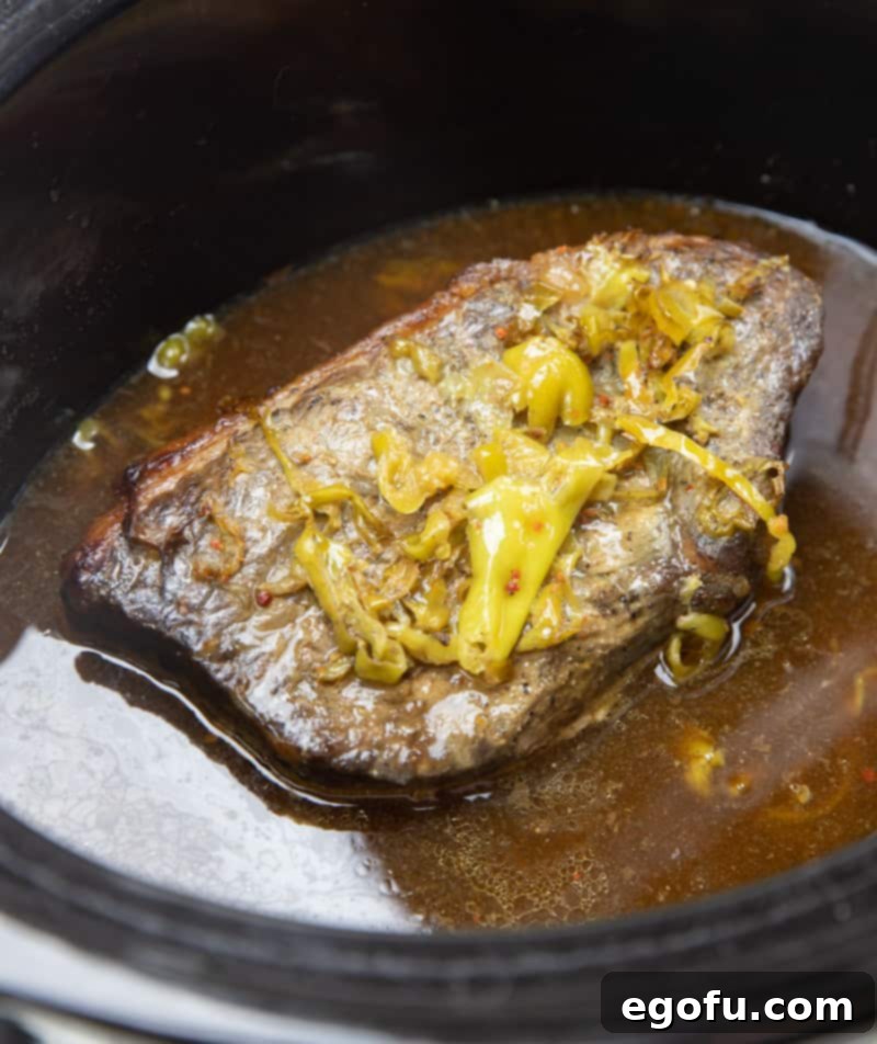A whole chuck roast cooking in a slow cooker, surrounded by savory juices.