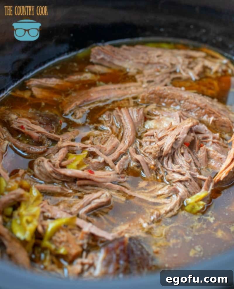 Shredded Italian beef soaking in its juices in a 6-quart crock pot, ready for serving.