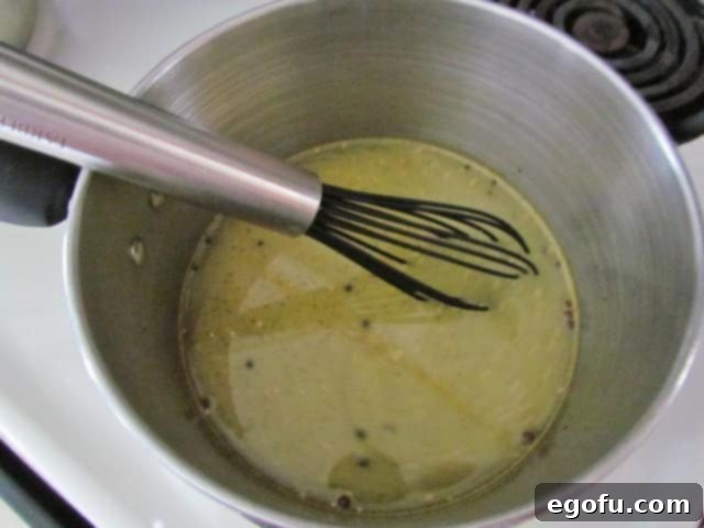 Sweet & Tangy Golden Slices 14 A whisk blending bread and butter seasoning mix with white vinegar in a stainless steel saucepan, creating the base for the pickling brine.