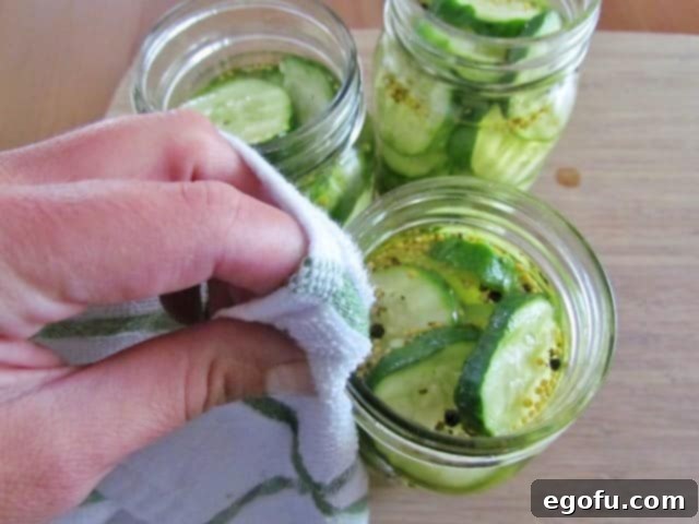 Sweet & Tangy Golden Slices 19 A hand carefully wiping the rim of a mason jar with a clean towel, a critical step to ensure a perfect seal for canning homemade pickles.