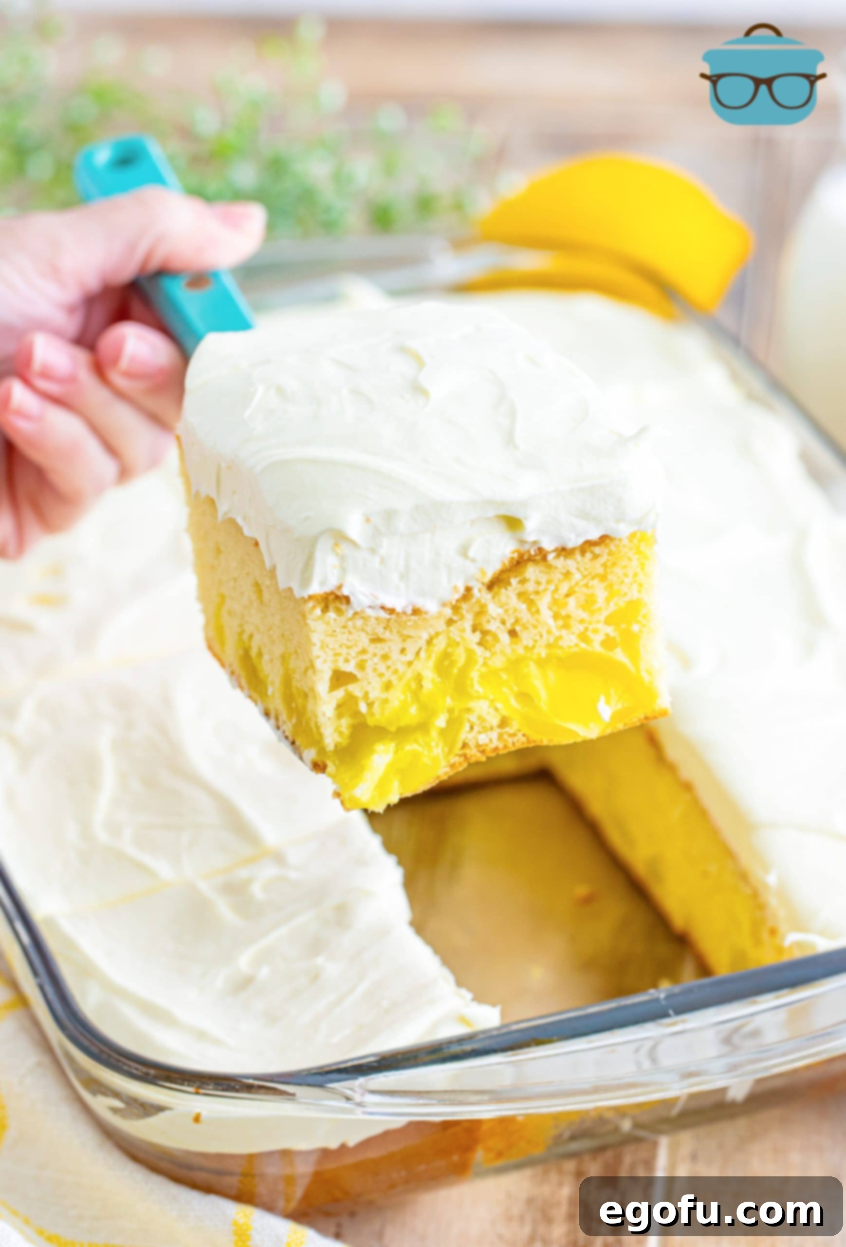 A slice of the frosted Lemon Dream Cake being gently lifted and removed from the baking dish, revealing the remaining cake and its inviting layers.