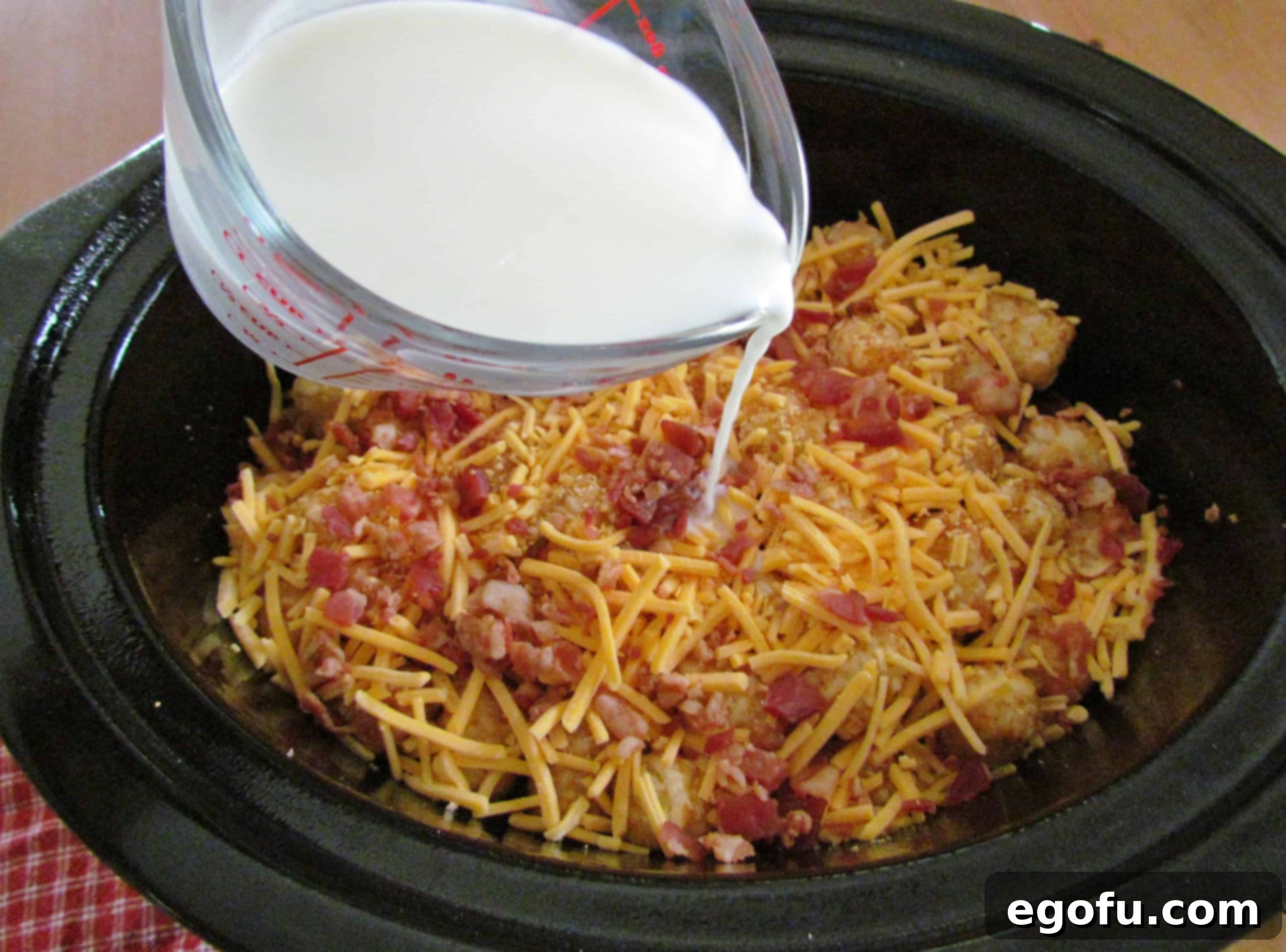 Milk being poured slowly and evenly over the top layers of the tater tot casserole in a slow cooker.