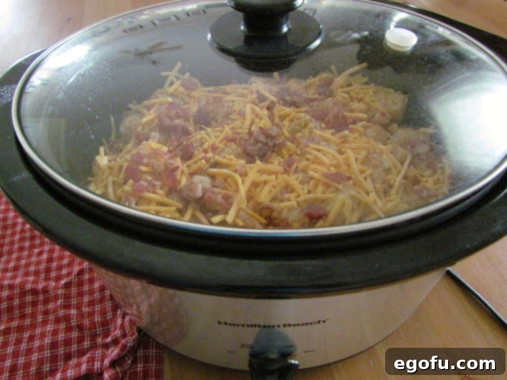 A black oval slow cooker, covered and cooking, with all the chicken tater tot casserole ingredients simmering inside.