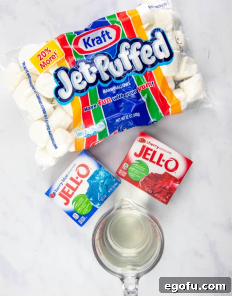 A flat lay showing jumbo marshmallows, berry blue Jell-O, strawberry Jell-O, a glass of water, and toothpicks, all ingredients for the patriotic treat.