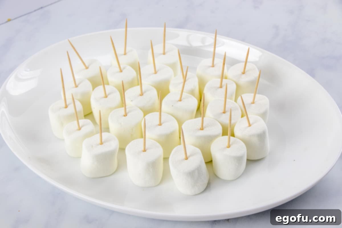 Toothpicks securely inserted into jumbo marshmallows, arranged neatly on a plate, ready for dipping.