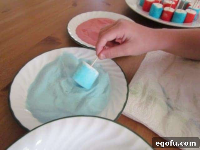 A marshmallow being rolled in Berry Blue Jell-O powder on a plate, creating a vibrant blue coating.
