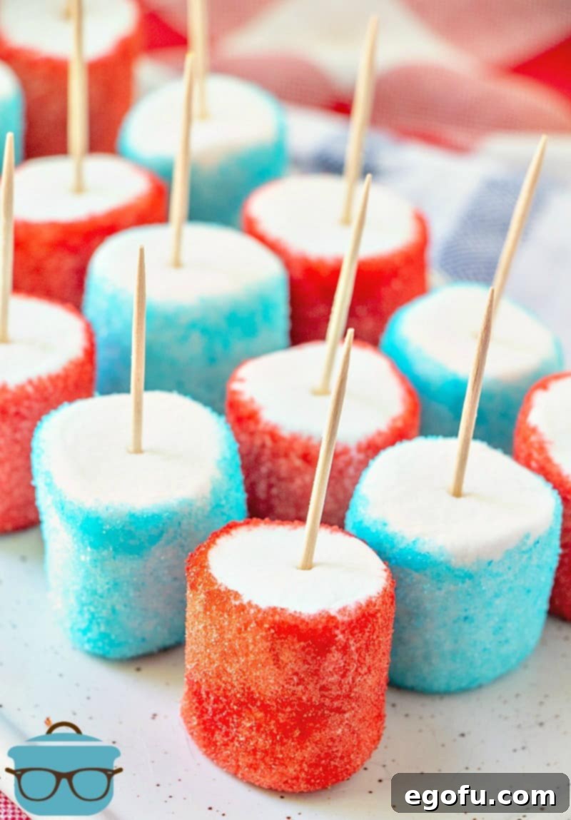 Close-up of red and blue Jell-O dipped marshmallows with toothpicks inserted, presented on a white tray, showcasing their vibrant colors and crust.