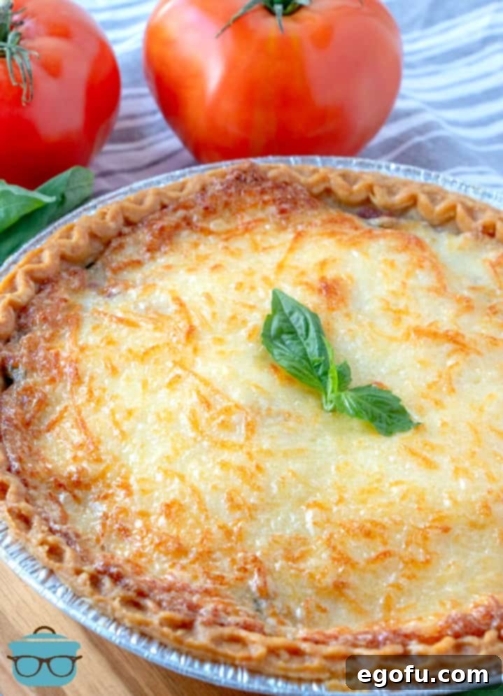 fully cooked, Bacon Tomato Pie topped with a sprig of fresh basil with whole tomatoes pictured Iin the background