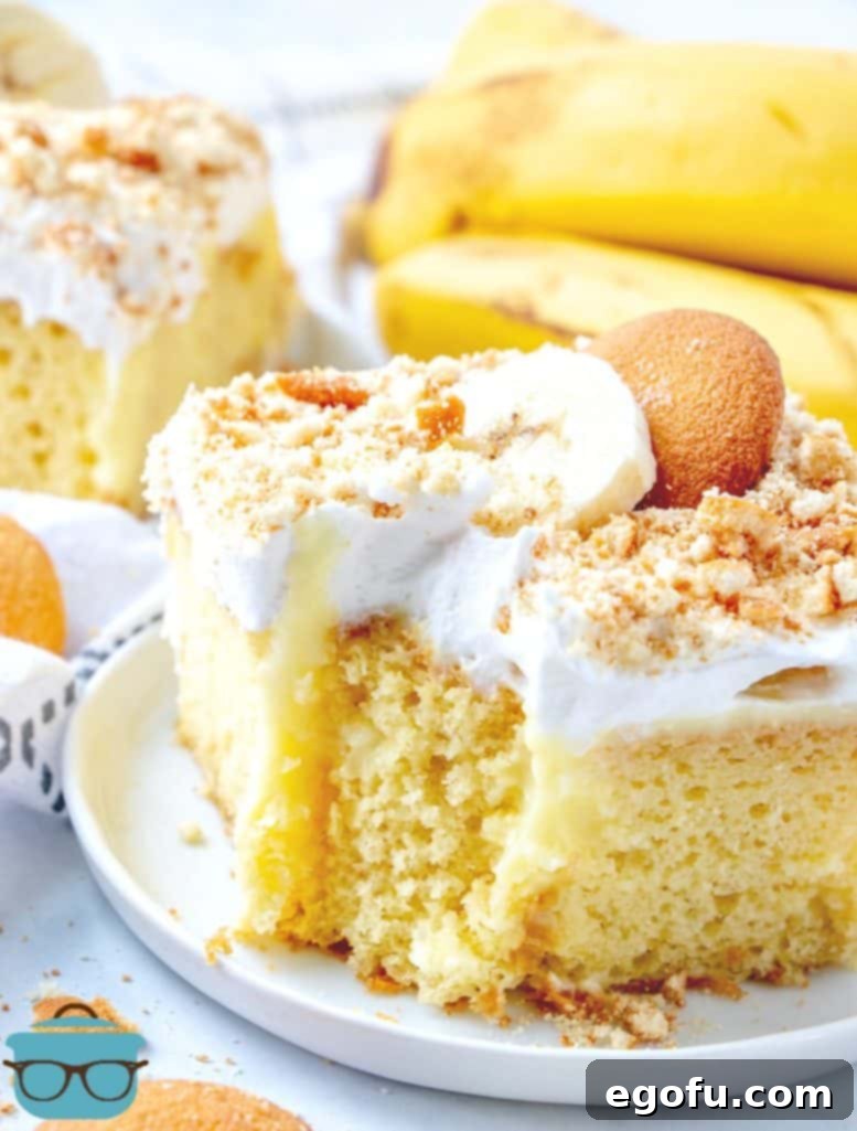 A close-up of a slice of Banana Pudding Poke Cake, showcasing its moist texture and layered components with a visible bite taken out.