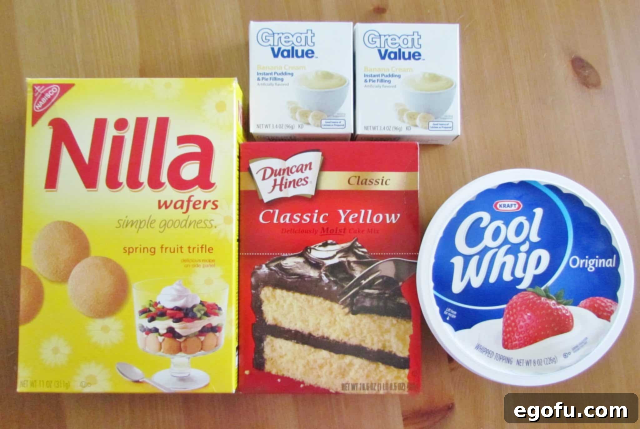 A flat lay photograph showcasing all the ingredients needed to make the Banana Pudding Poke Cake: yellow cake mix, Nilla wafers, instant vanilla pudding, Cool Whip, and fresh bananas.