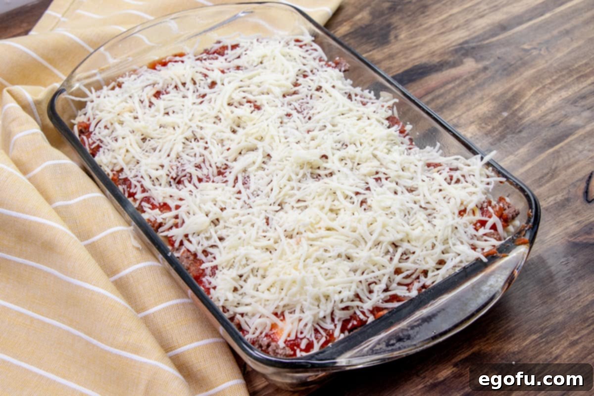 Shredded cheese generously added on top of the final layers of the ravioli casserole in the baking dish.