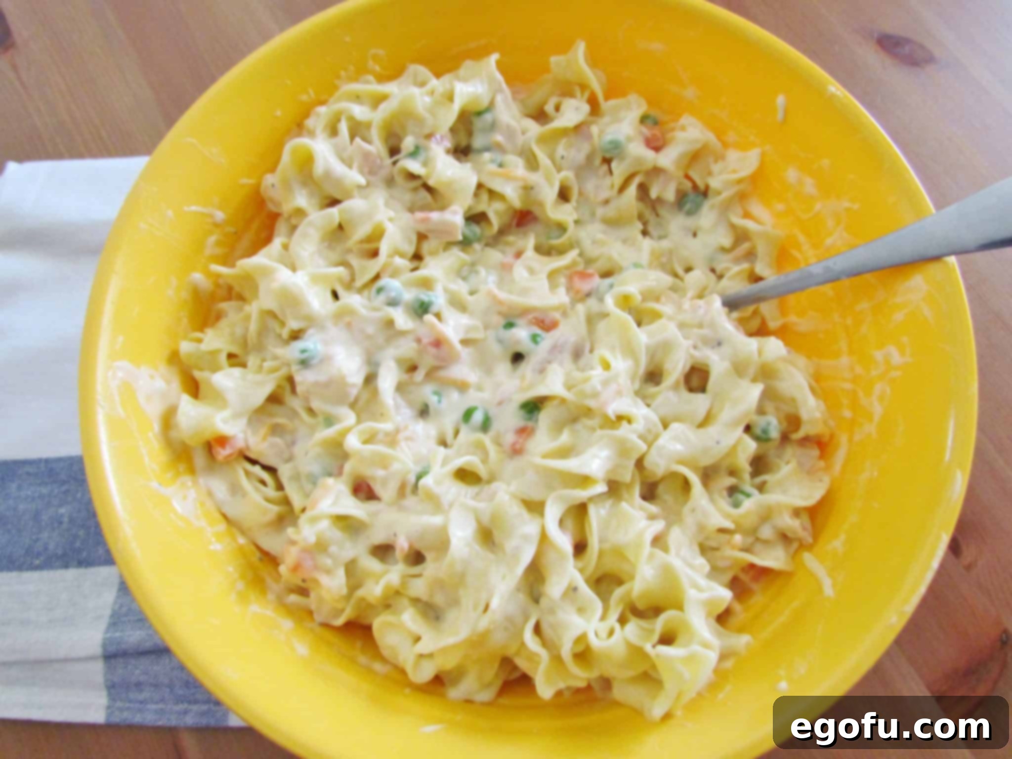 Cooked egg noodles stirred into the creamy chicken and vegetable mixture in a bowl.