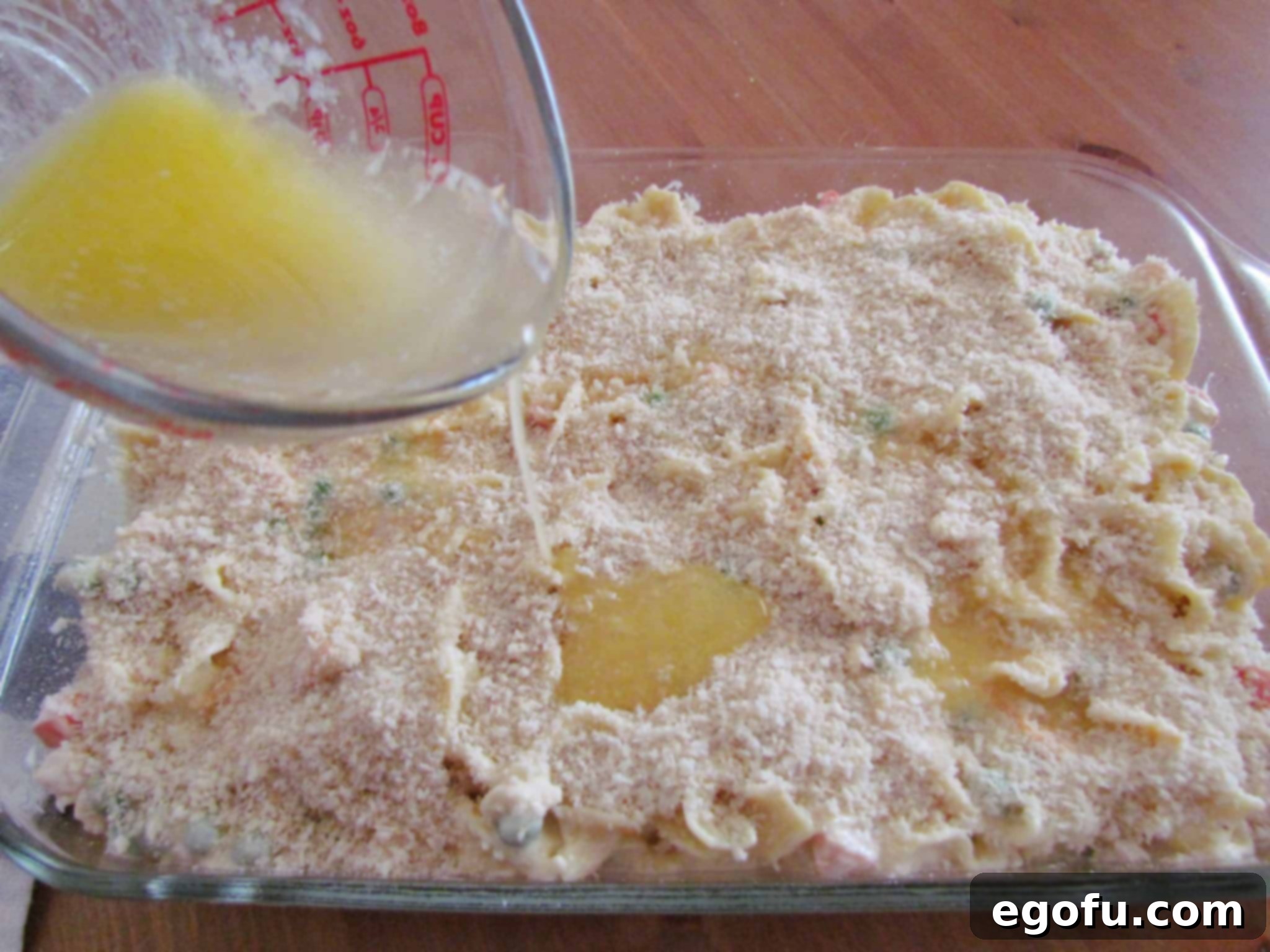 Pouring melted butter evenly over the panko bread crumbs topping on the casserole.