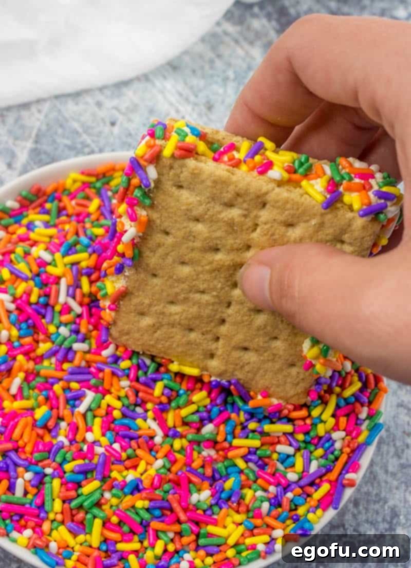 Finished graham cracker and frosting sandwiches, with colorful sprinkles on the sides, arranged neatly on a cookie sheet before freezing.