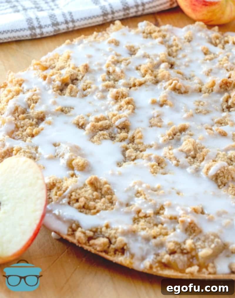 Easy Apple Dessert Pizza presented whole on a rustic wooden cutting board, with a sliced apple resting alongside, highlighting its fresh, homemade appeal.