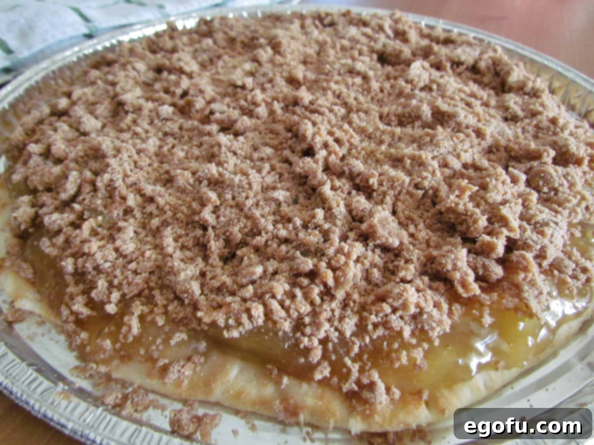 The rich brown sugar crumble topping is evenly sprinkled over the spiced apple pie filling, covering the entire pizza crust, ready for baking.