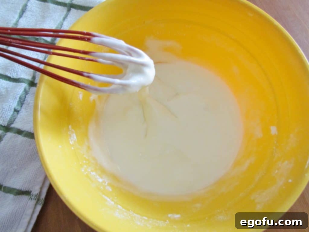 Powdered sugar and milk are whisked together in a small yellow mixing bowl, creating a smooth and sweet icing for the dessert pizza.
