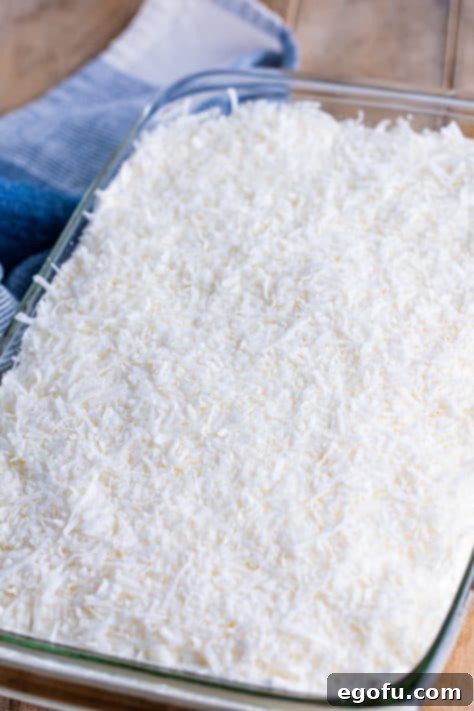 shredded coconut flakes put on top of whipped topping on cake.