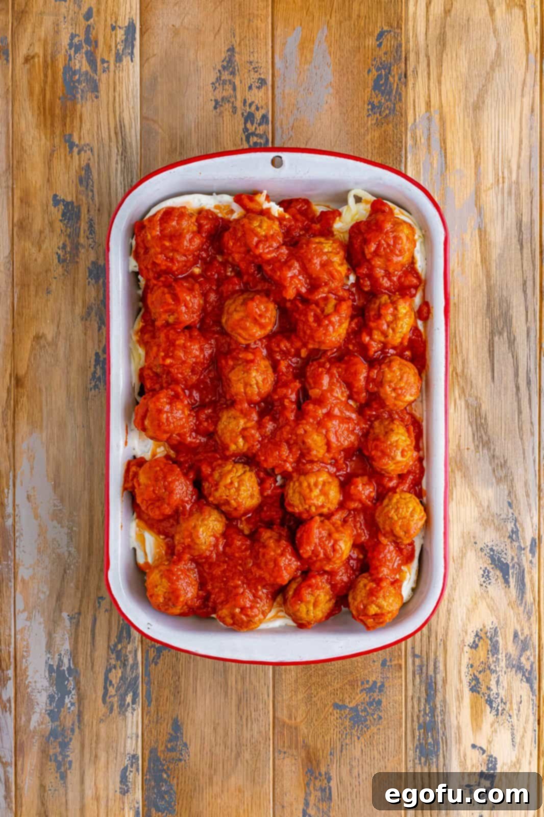 Pasta sauce and meatballs shown spread out on top of the cheese layer in the casserole dish.