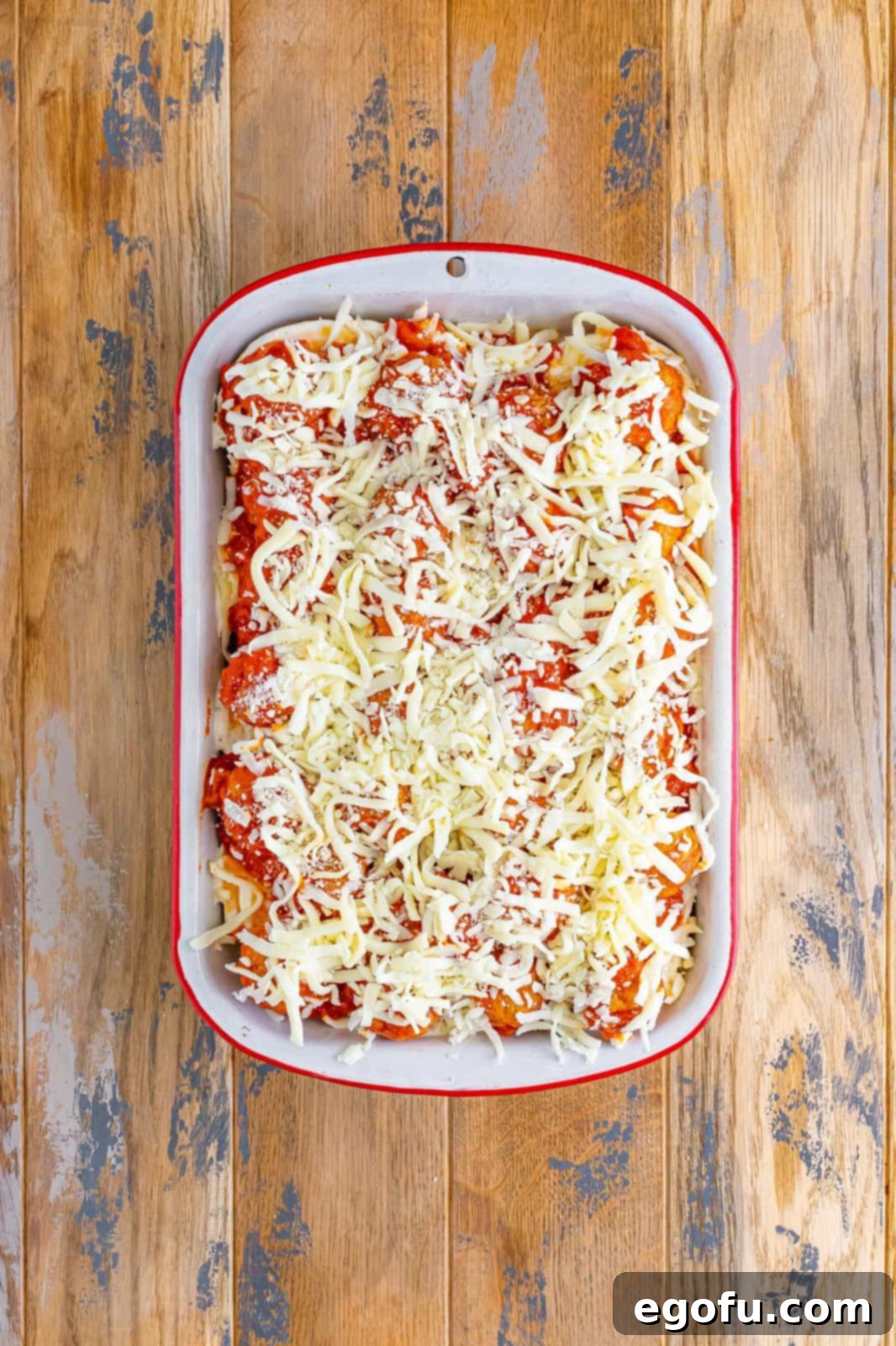 Remaining shredded cheese shown sprinkled on top of the meatball and sauce layer in the casserole.