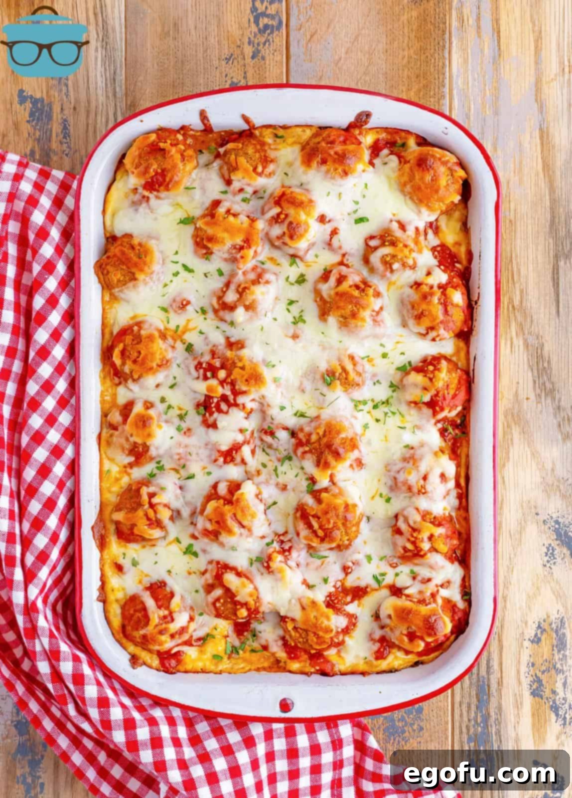 Overhead photo of a fully cooked, bubbling Meatball Sub Casserole in the baking dish on a wooden surface.
