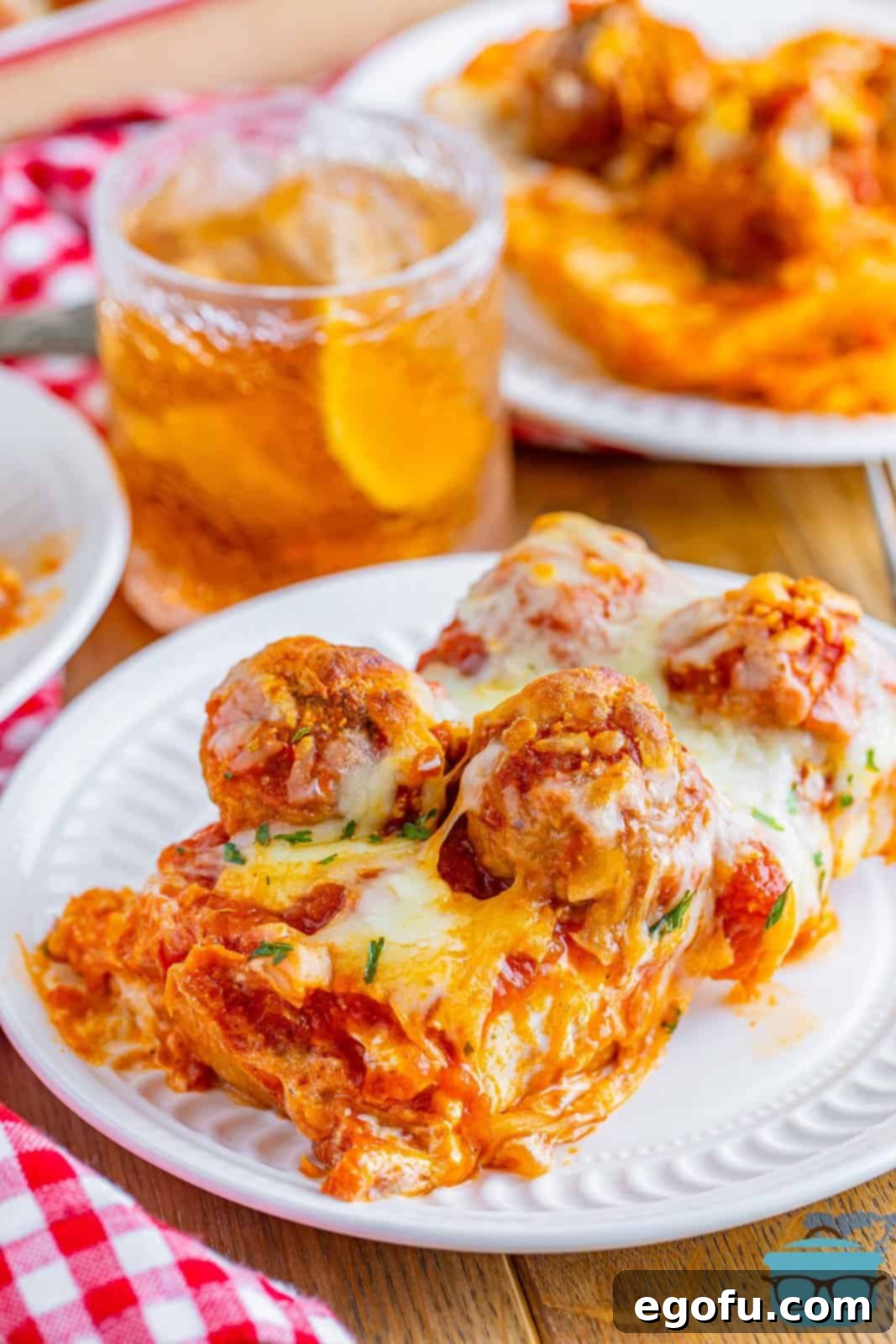 A slice of Meatball Sub Casserole shown on a white plate with a glass of iced tea in the background, ready to eat.