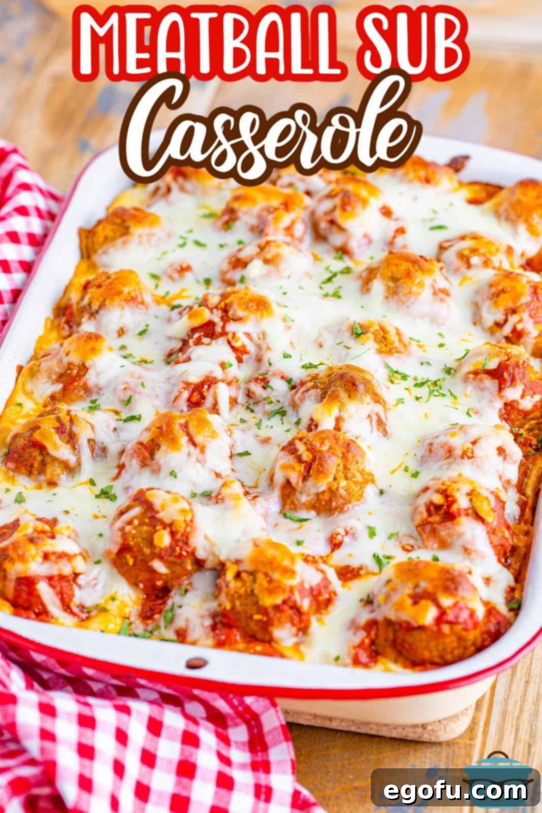 Meatball Sub Casserole shown fully baked in a white and red casserole dish with a red and white dishcloth on the side, ready to be served.