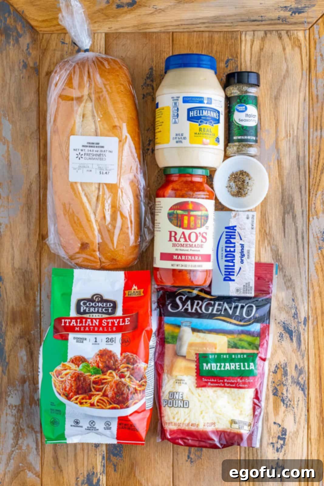 A flat lay image showing all the ingredients for Meatball Sub Casserole: Italian bread, mayonnaise, pasta sauce, salt, pepper, Italian seasoning, cream cheese, Italian style meatballs, and mozzarella cheese.