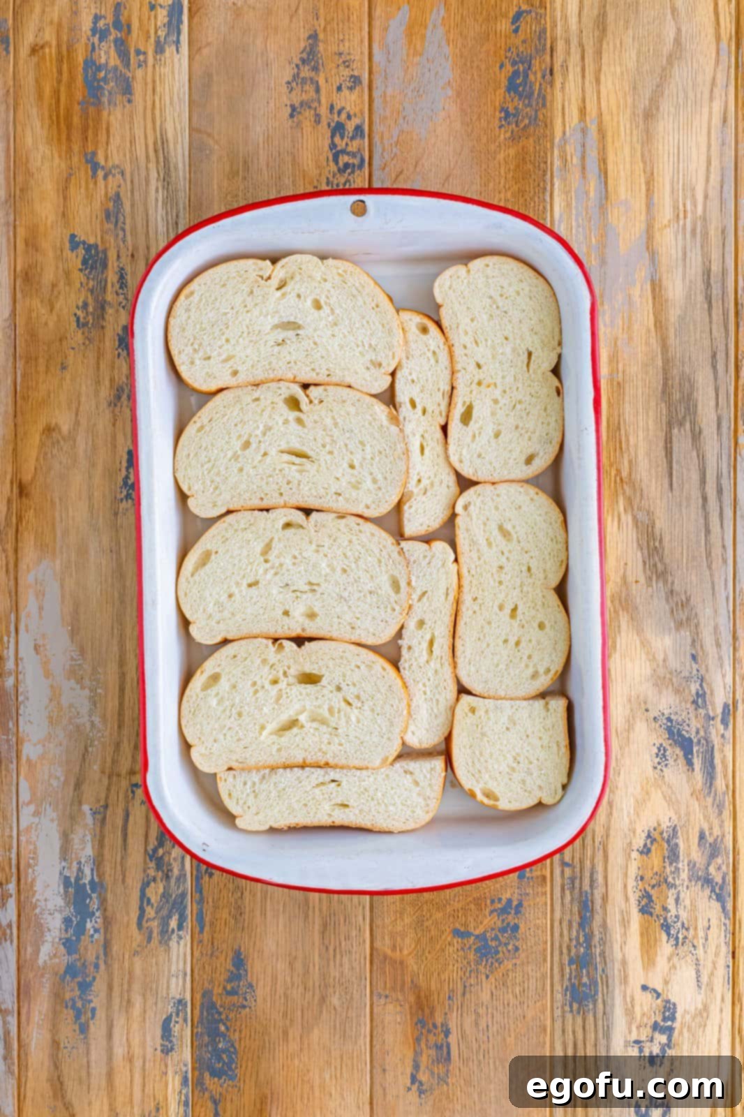 Sliced Italian bread shown arranged in an even layer in a baking dish, forming the base of the casserole.