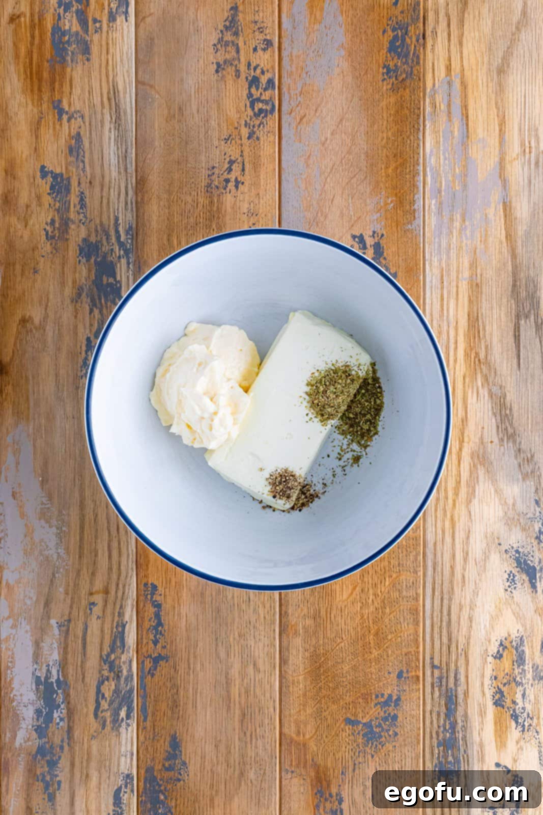 Cream cheese, Italian spices, and mayonnaise shown mixed together in a white bowl, ready to be spread.