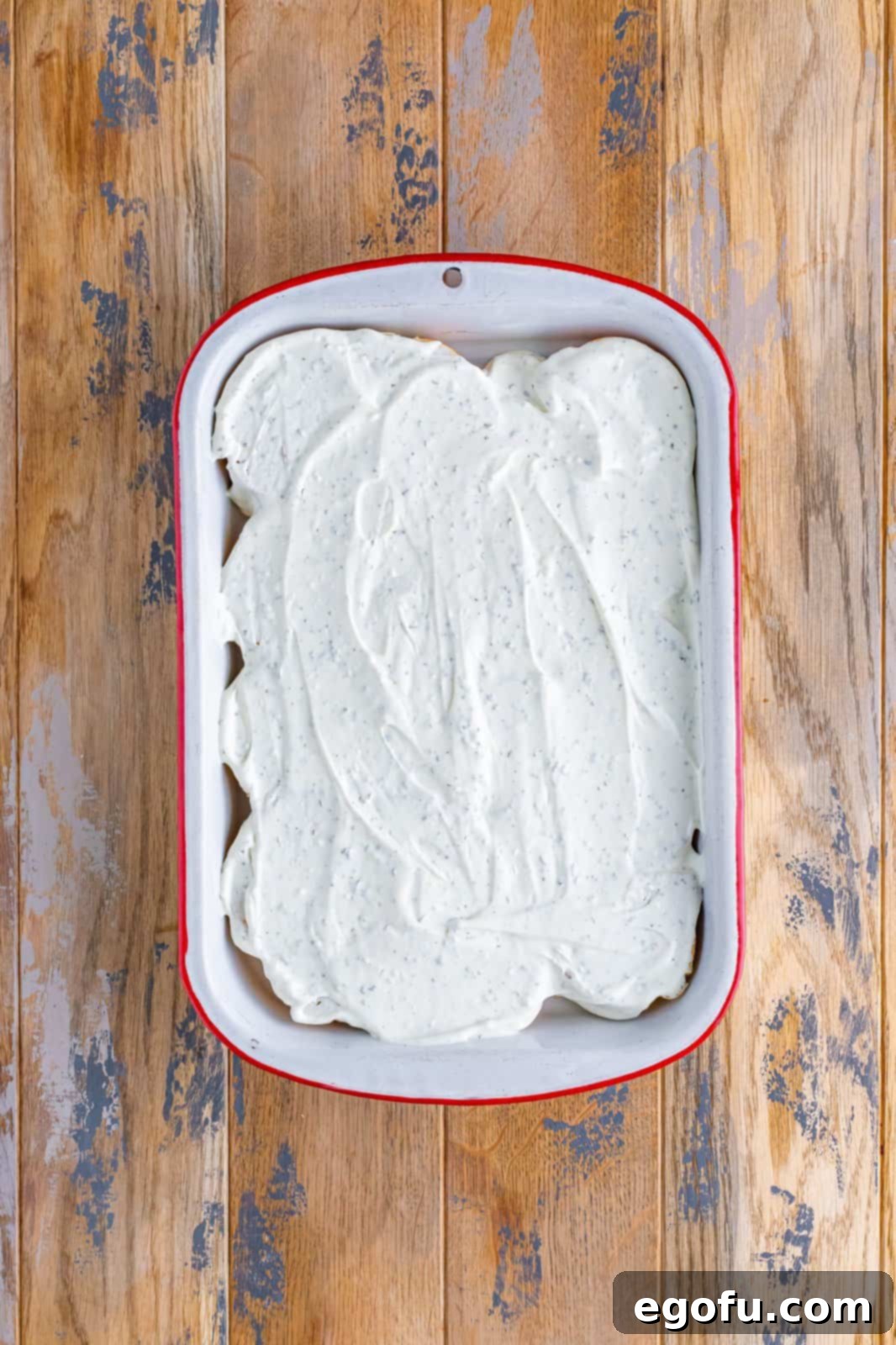 Cream cheese mixture shown smoothly spread over the bread slices in the baking dish.