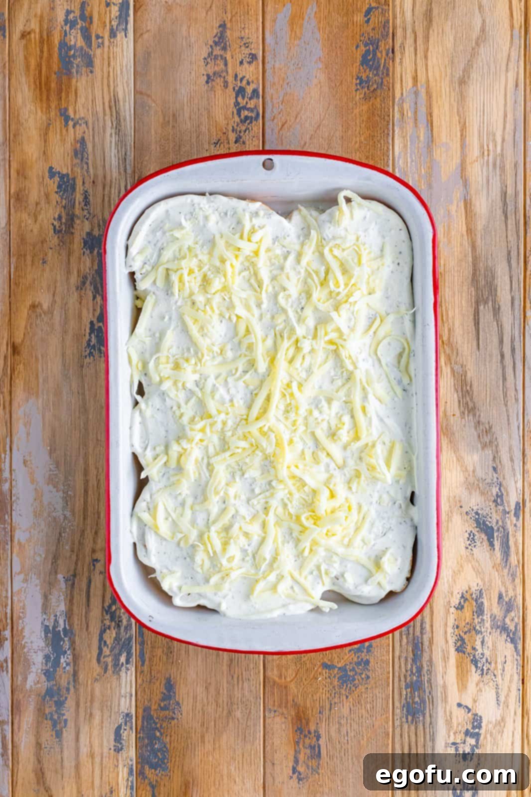 Shredded mozzarella cheese shown sprinkled over the cream cheese layer in the casserole dish.