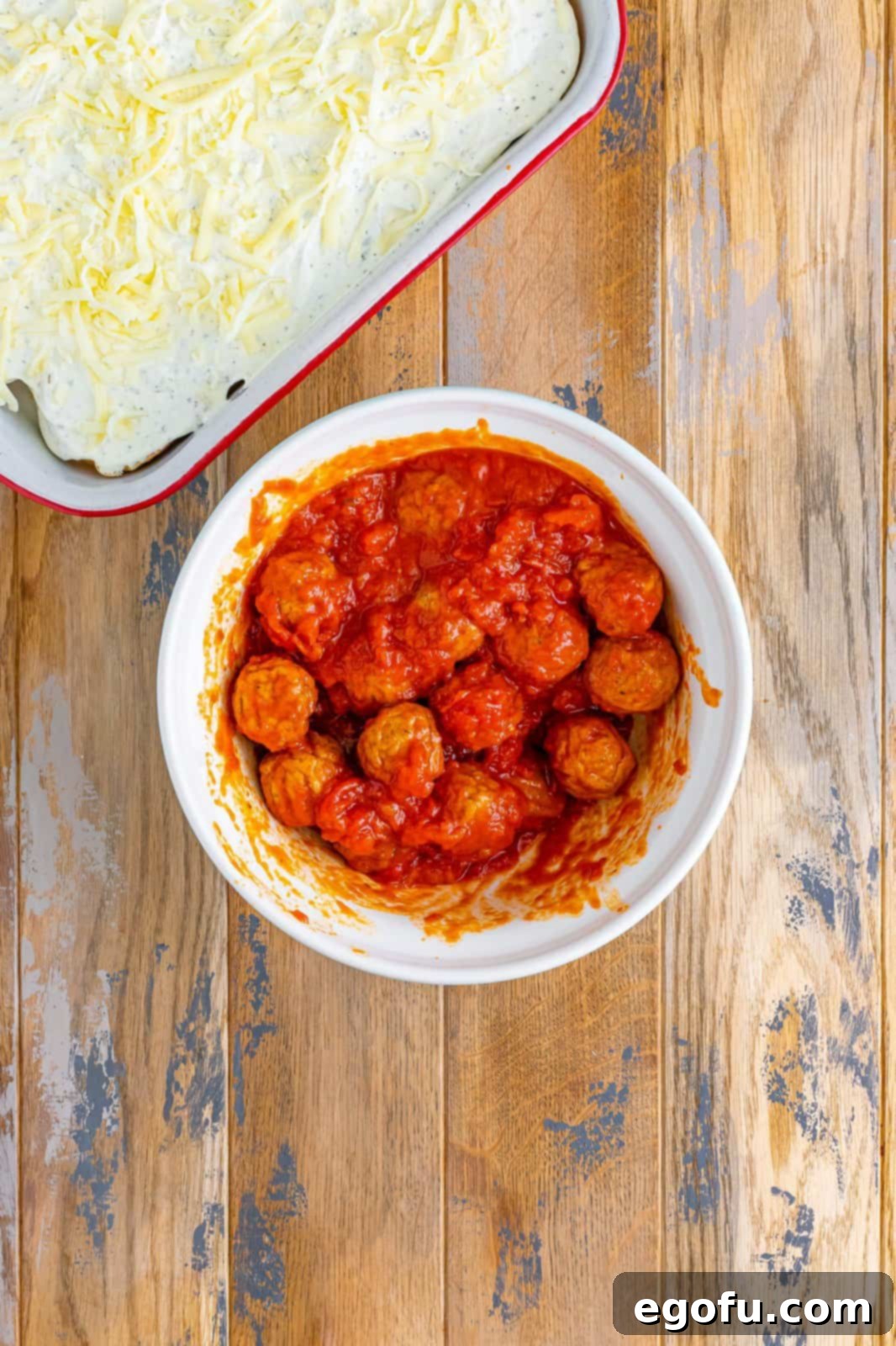 Thawed Italian style meatballs shown mixed together with pasta sauce in a white bowl, ready for the casserole.