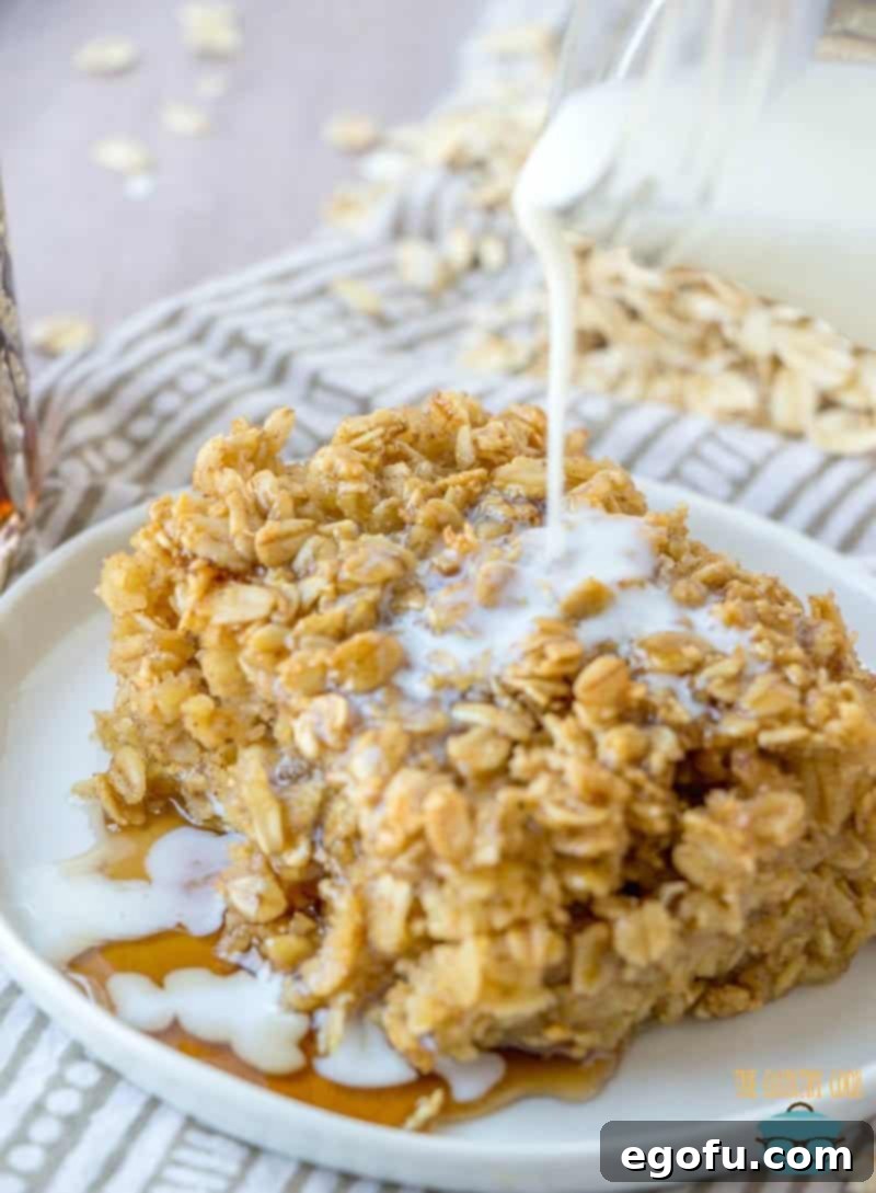 A close-up of a slice of Maple Brown Sugar Baked Oatmeal, with a gentle stream of warm milk being drizzled over it, adding a creamy, comforting touch.