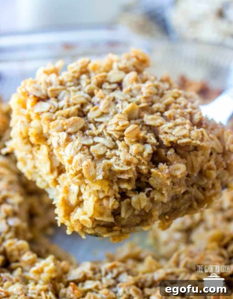 A hand holding up a perfectly baked, rectangular slice of Maple Brown Sugar Baked Oatmeal, showing its tender, slightly crumbly texture, ready to be placed on a plate.