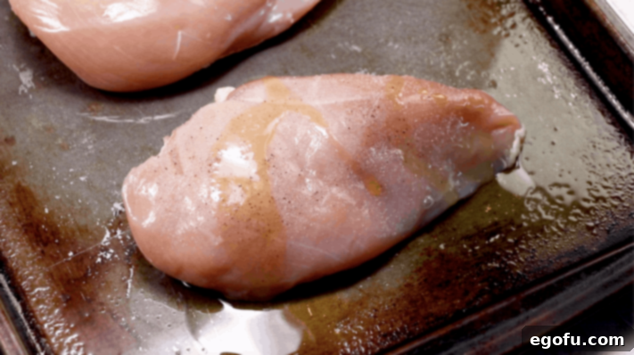 chicken breast on a baking sheet drizzled with olive oil