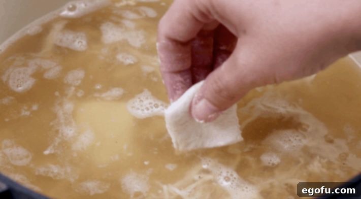 dropping individual dumplings into chicken broth