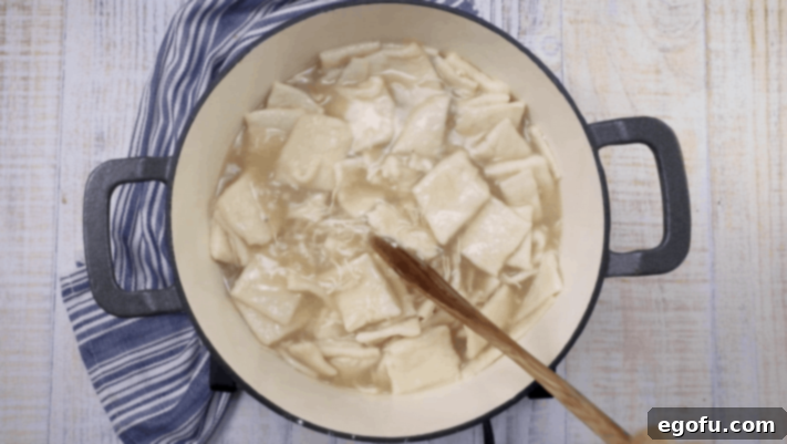 pot full of chicken and dumplings with a blue kitchen towel set to the side