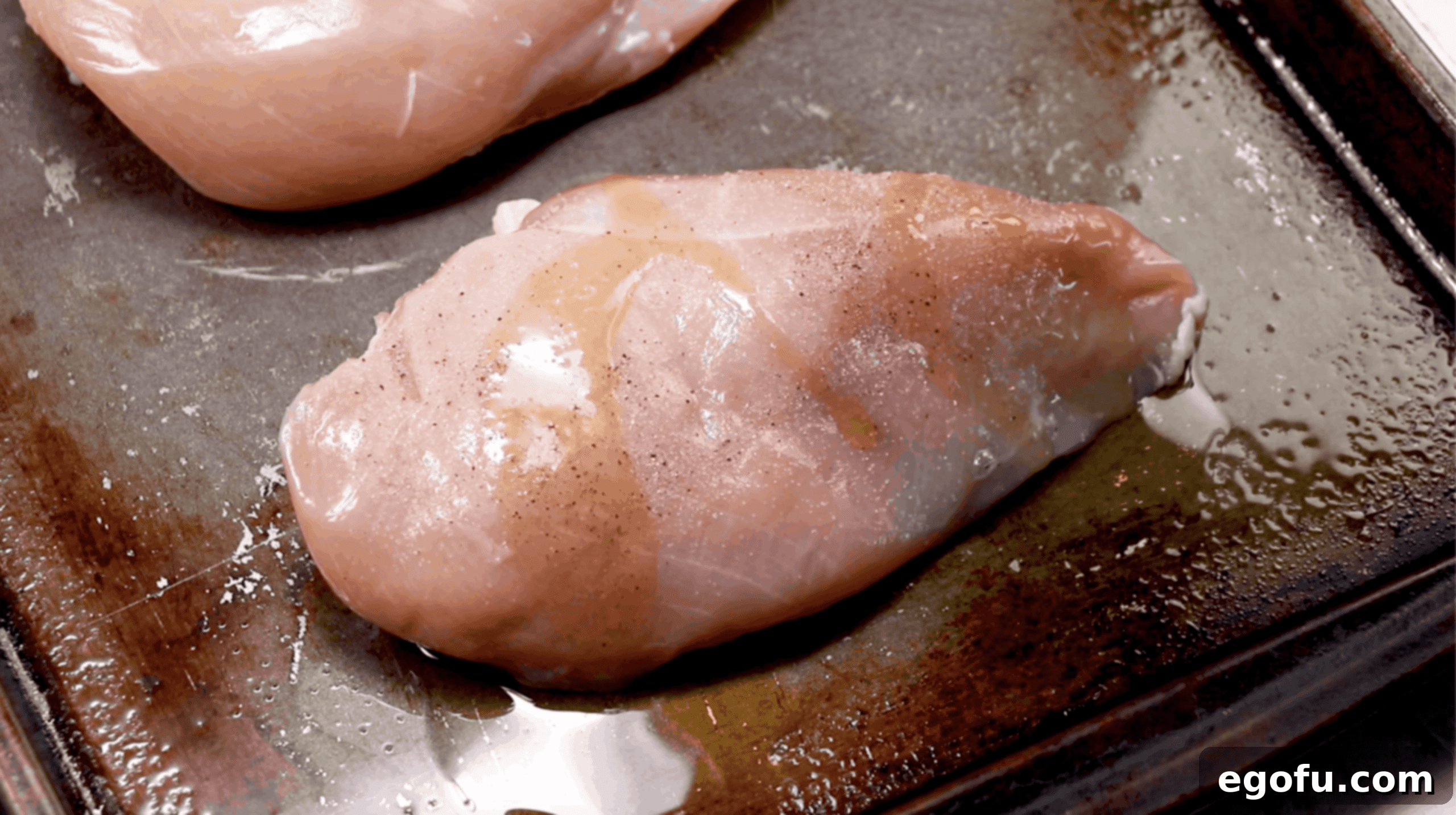 chicken breast on a baking sheet drizzled with olive oil