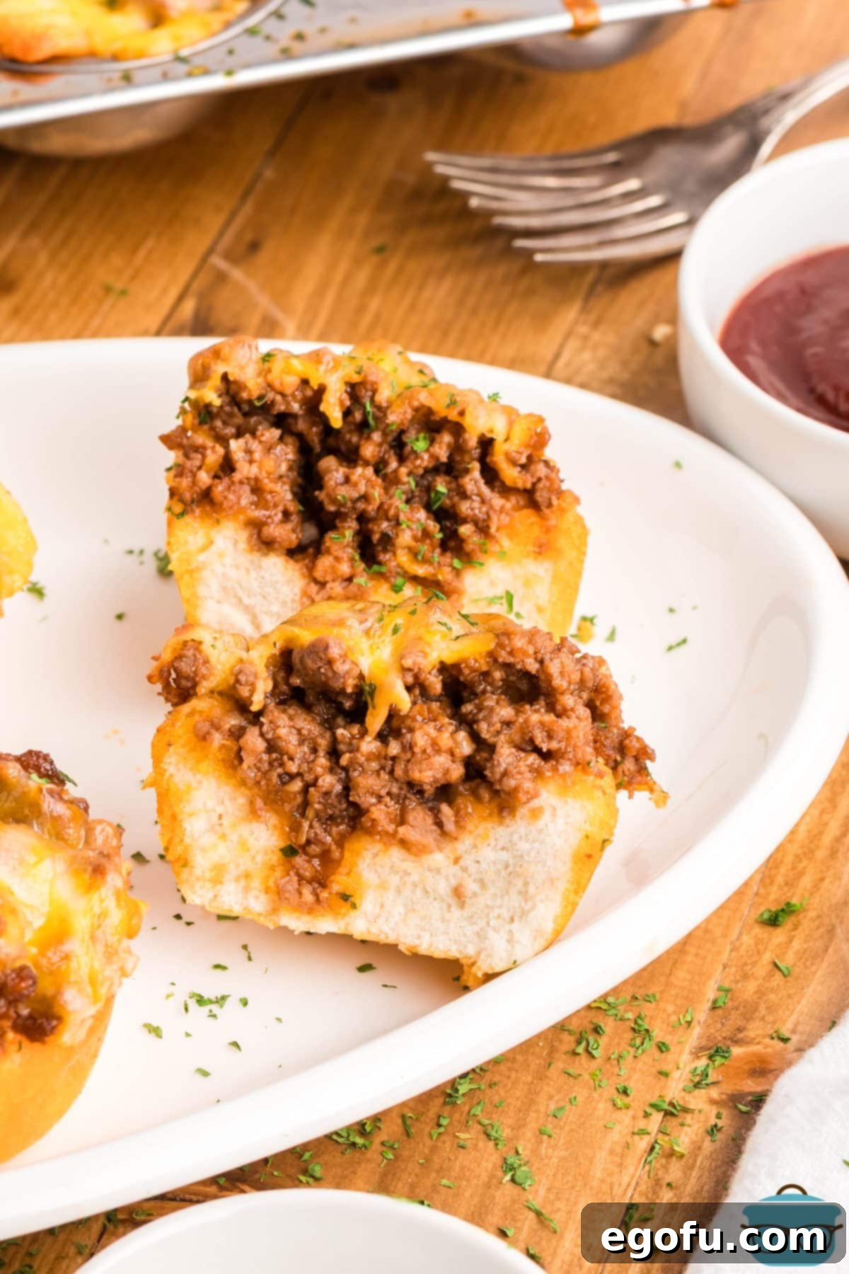Smoky Beef Biscuit Pockets 9 A BBQ Beef Biscuit Cup cut in half and placed on a white plate, revealing the savory ground beef and melted cheese filling inside the flaky biscuit crust.