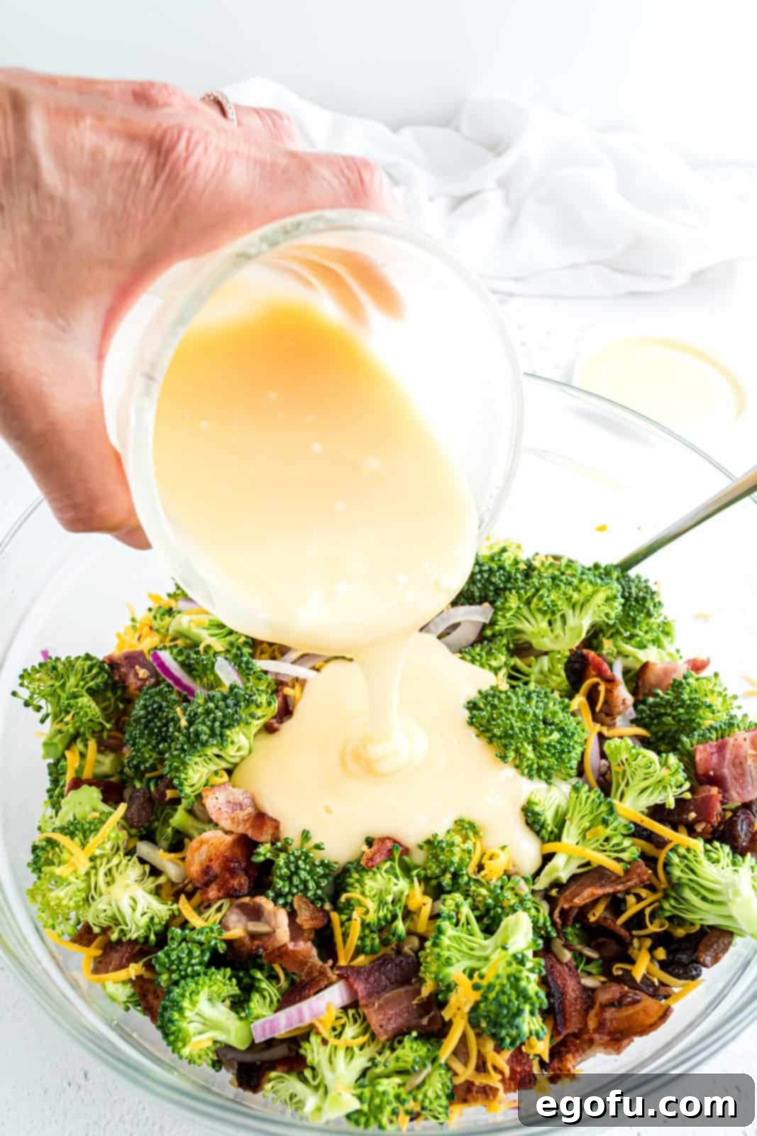 The creamy dressing being poured over the mixed salad ingredients in a large bowl.