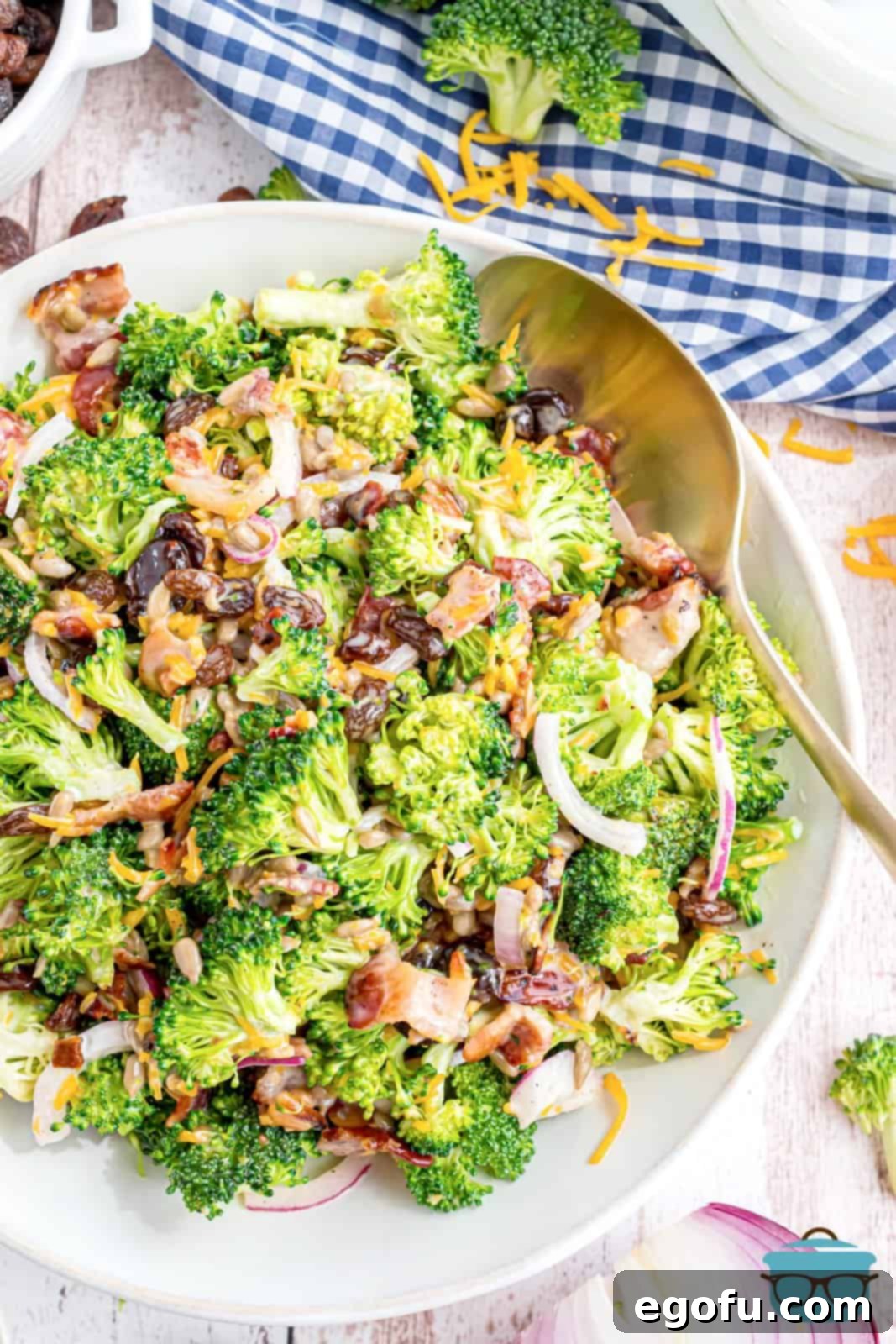 A fully combined broccoli salad in a shallow white bowl with a silver serving spoon, ready to be enjoyed.