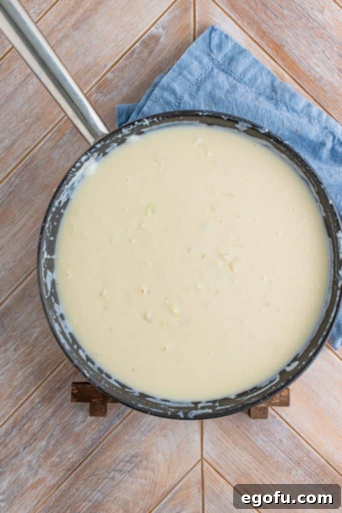 A thick and creamy white sauce bubbling in a large skillet, indicating it has reached the desired consistency for the pot pie filling.