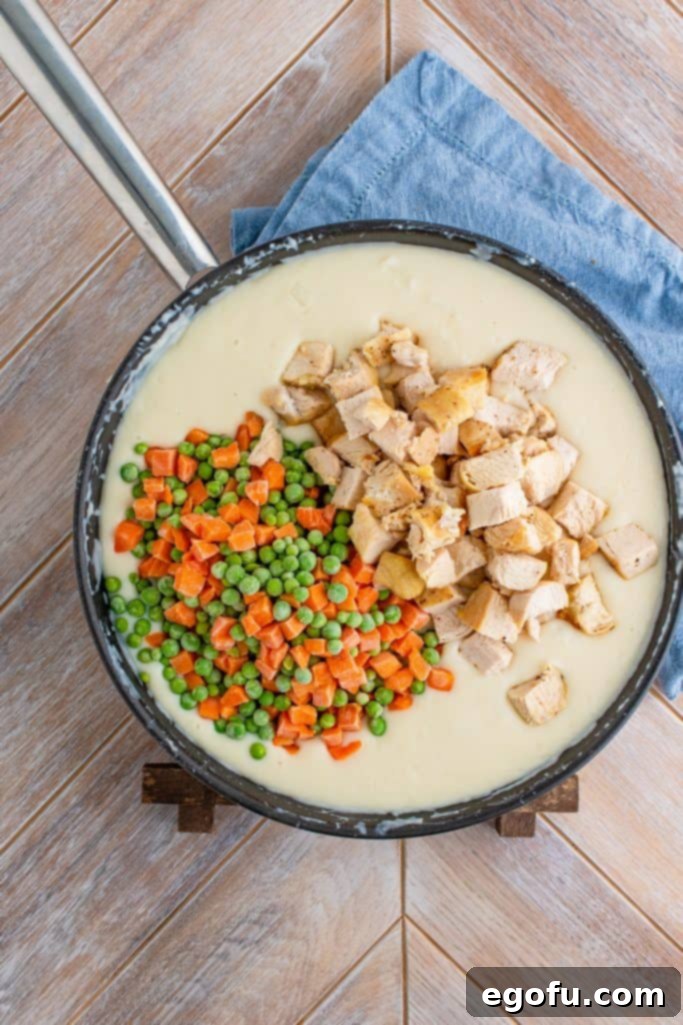 Cooked, cubed chicken and frozen peas and carrots stirred into the thick, creamy pot pie filling in a large skillet.