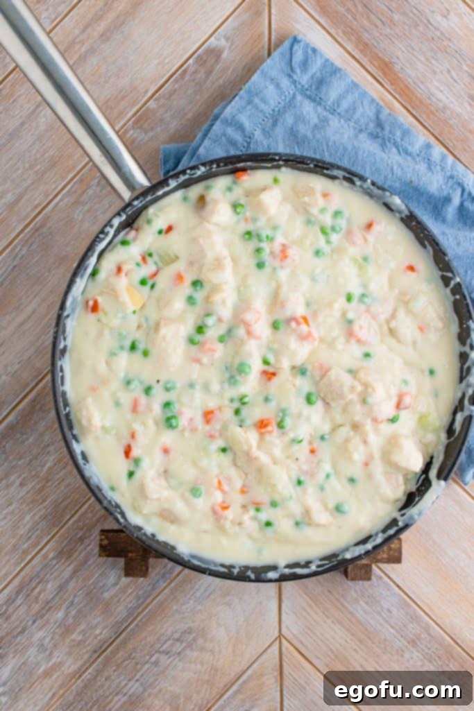 The finished chicken pot pie filling, rich and creamy with chicken and vegetables, gently simmering in a large skillet.