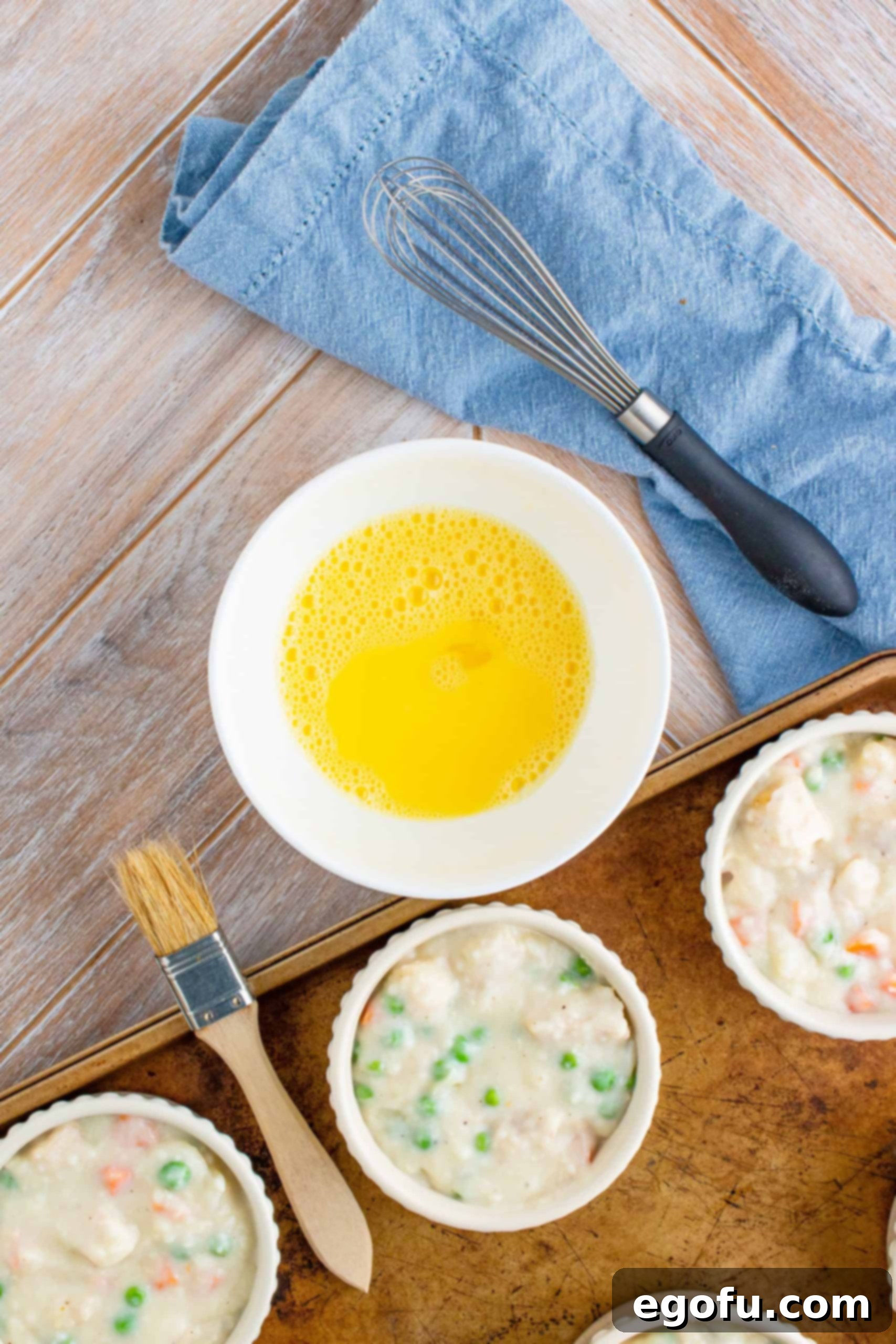 A small white bowl containing an egg and water, whisked together to form an egg wash.