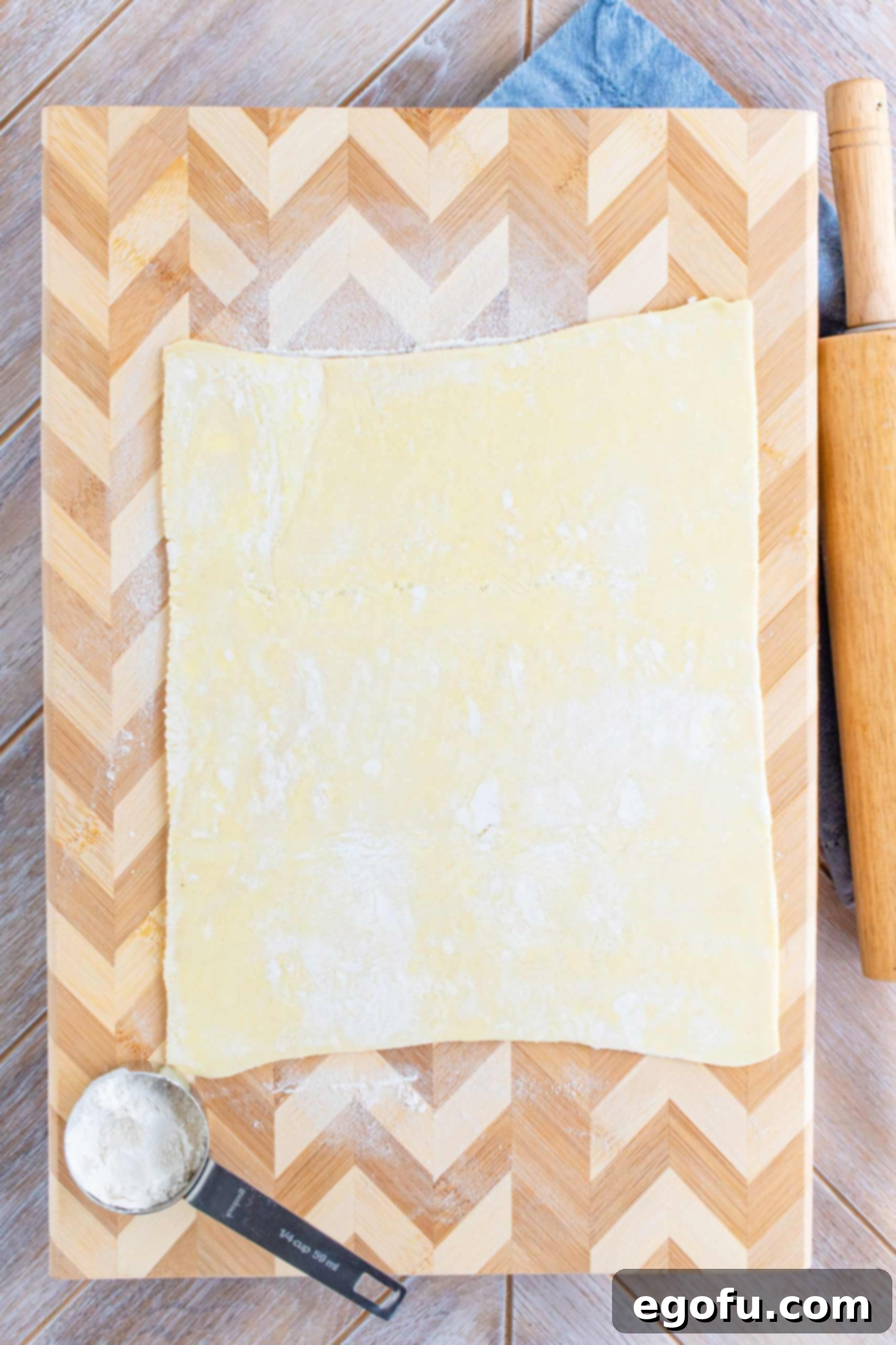 A rolled-out sheet of puff pastry on a floured surface, with visible seams smoothed out, ready for cutting.