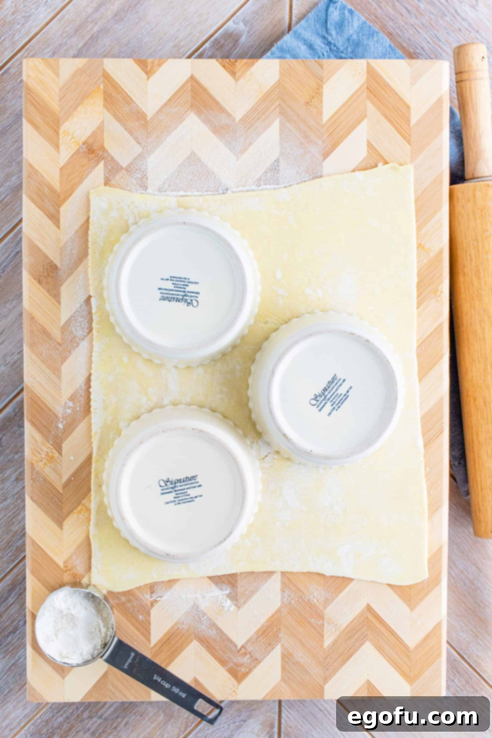 Several white ramekins placed upside down on a sheet of puff pastry, with cuts made around them to form pastry circles with an overhang.