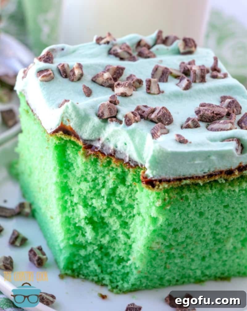 Effortless Grasshopper Indulgence 2 A perfectly sliced piece of vibrant green Grasshopper Cake, showcasing its minty layers, rich chocolate fudge, and fluffy whipped topping, garnished with Andes mint chocolate candies, served on a white plate with a fork beside it.