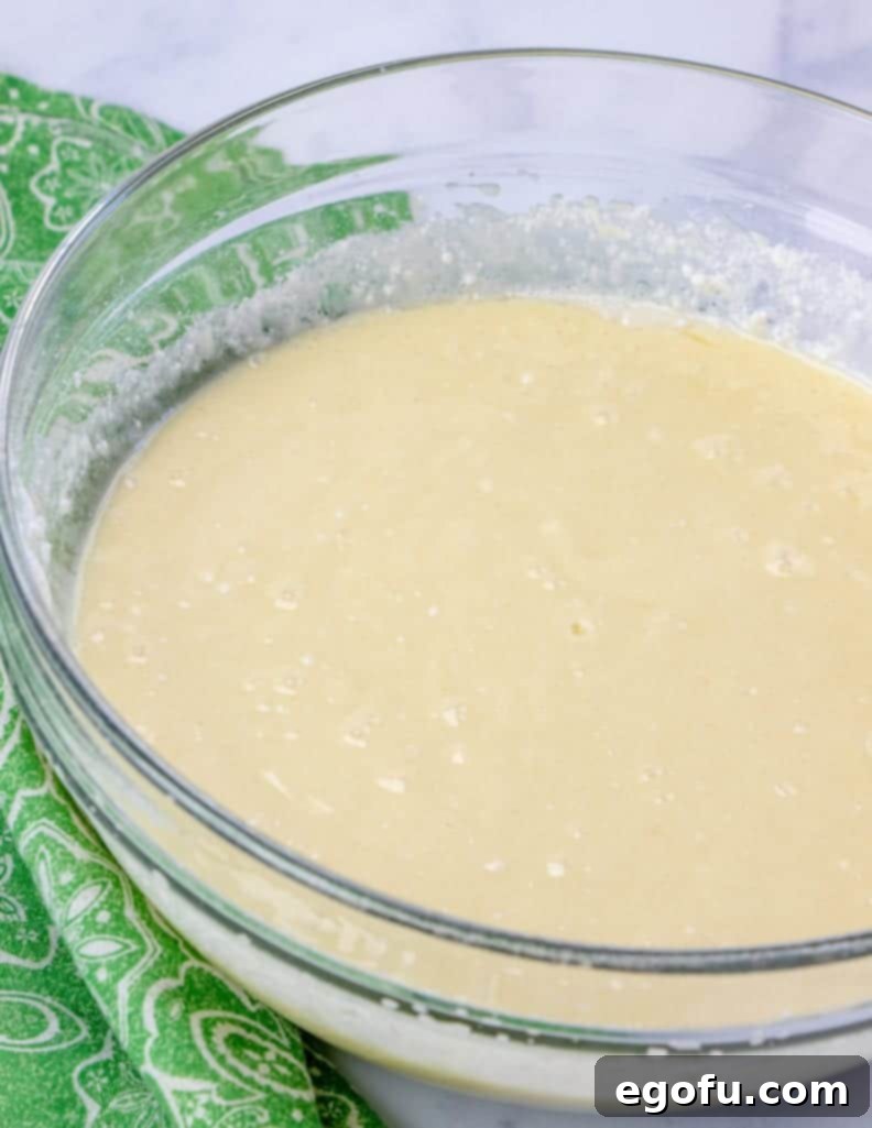 Effortless Grasshopper Indulgence 5 Mint extract being poured into a bowl of prepared white cake batter, ready for mixing.